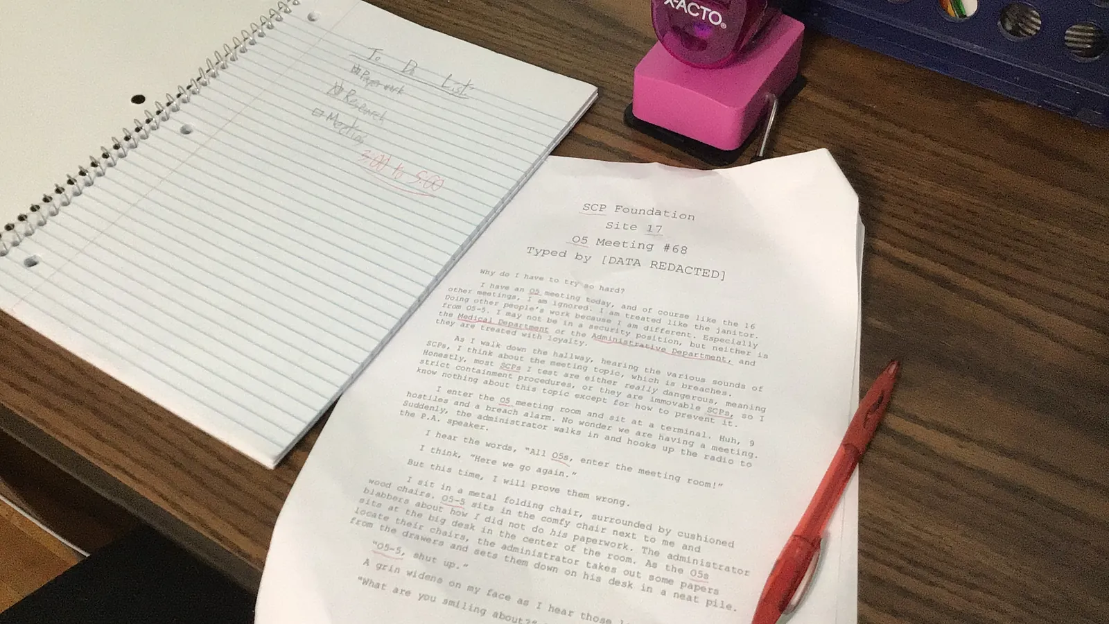 Handwritten and printed papers on a desk next to a notebook and a pen