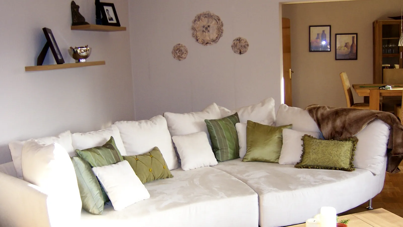 An apartment living room with a white sofa, cushions and shelves on the wall