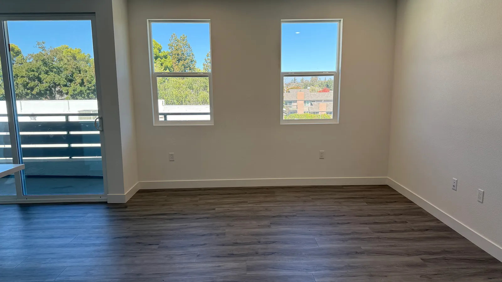 An empty apartment room with wooden flooring and windows looking out on trees