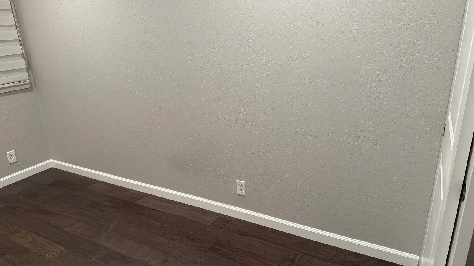 An empty, clean apartment room with white walls and a dark wooden floor